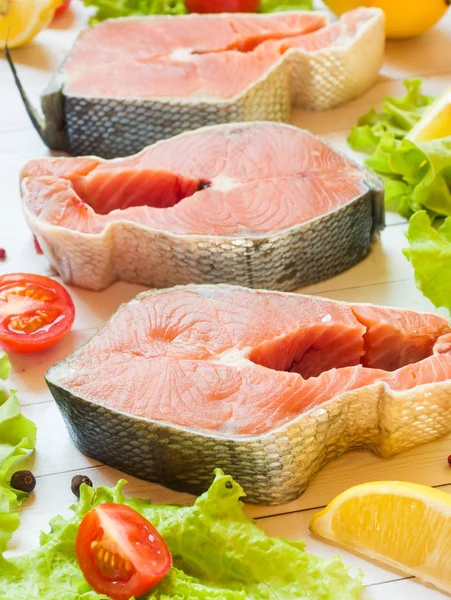 Стейк из сырой красной рыбы с лимоном и специями и свежими овощами на светлом фоне . — стоковое фото
