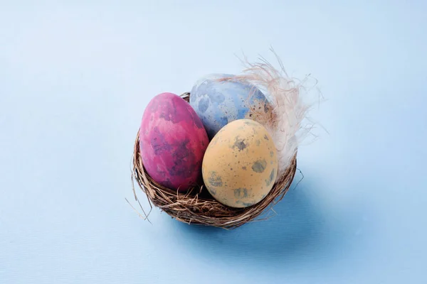 Uovo di Pasqua colorato nel nido su sfondo blu con spazio per la copia. Sfondo pasquale. Minimalismo — Foto Stock