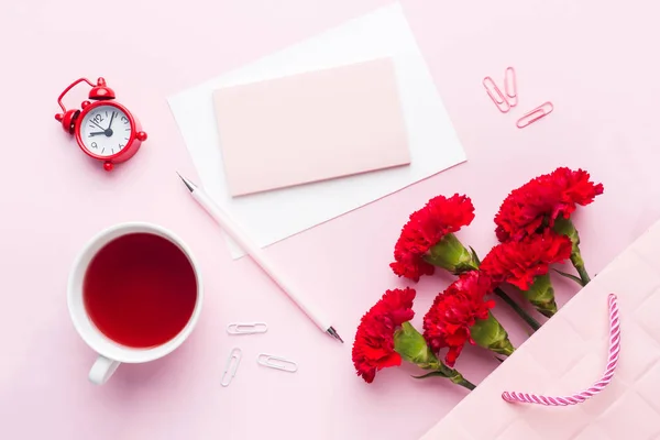 Rot-rosa Objekte. Tasse Tee, Nelkenblumen Notizblock für Text auf pastellrosa Hintergrund. Kopierraum. von oben flach liegend — Stockfoto
