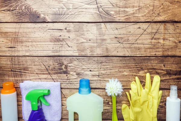 Bottles with detergents, brushes and sponges on wooden background. Colorful cleaning products. Home cleaning concept. Top view, copy space. — Stock Photo, Image