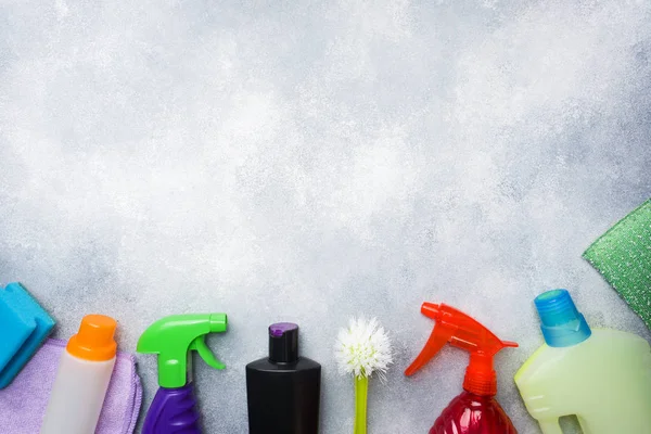 Bottles with detergents, brushes and sponges on concrete background. Colorful cleaning products. Home cleaning concept. Top view, copy space. — Stock Photo, Image