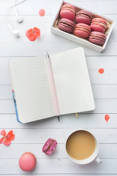 Tasse Kaffee, Makronenkekse in einer Schachtel, Blumen und ein Notizbuch auf weißem Hintergrund. Kopierraum. Konzept schönes Frühstück. flache Lage — Stockfoto