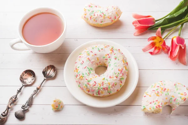 Cup of tea and donuts, flowers tulips on white table with copy space. — Stock Photo, Image