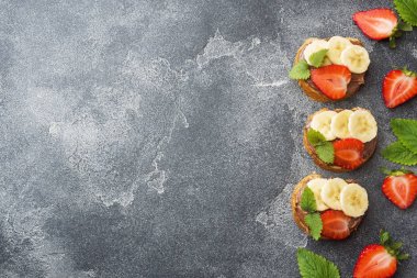 Çikolata nougat, çilek ve muz ile lezzetli sandviçler. Kahvaltı Kavramı. Koyu beton arka plan Kopyalama alanı