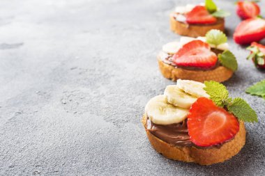 Çikolata nougat, çilek ve muz ile lezzetli sandviçler. Kahvaltı Kavramı. Koyu beton arka plan Kopyalama alanı