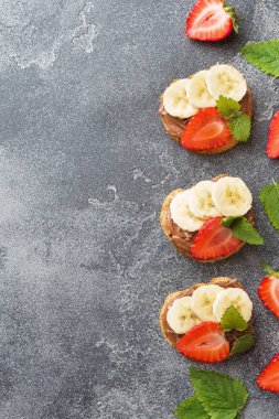 Çikolata nougat, çilek ve muz ile lezzetli sandviçler. Kahvaltı Kavramı. Koyu beton arka plan Kopyalama alanı