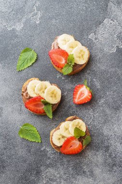 Çikolata nougat, çilek ve muz ile lezzetli sandviçler. Kahvaltı Kavramı. Koyu beton arka plan.
