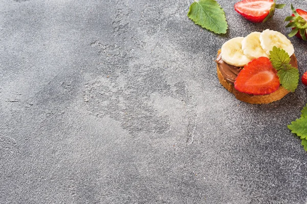 Çikolata nougat, çilek ve muz ile lezzetli sandviçler. Kahvaltı Kavramı. Koyu beton arka plan Kopyalama alanı