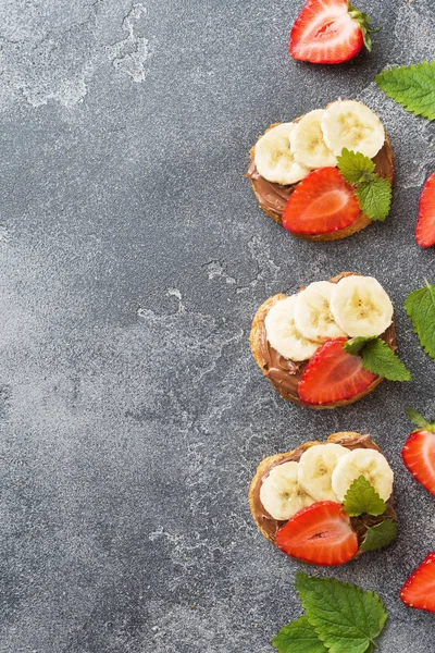 Çikolata nougat, çilek ve muz ile lezzetli sandviçler. Kahvaltı Kavramı. Koyu beton arka plan Kopyalama alanı