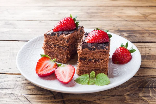 Chocolate truffle cake with strawberries and mint. Wooden table.