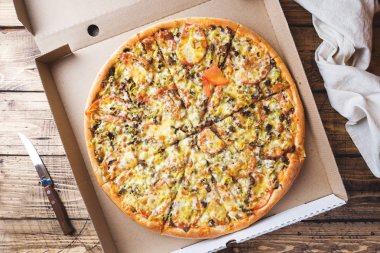 Ahşap bir masa üzerinde bir karton kutu içinde taze pişmiş pizza.