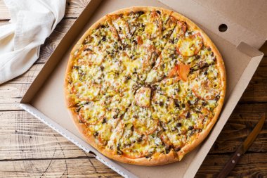 Ahşap bir masa üzerinde bir karton kutu içinde taze pişmiş pizza.