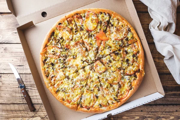 Ahşap bir masa üzerinde bir karton kutu içinde taze pişmiş pizza.