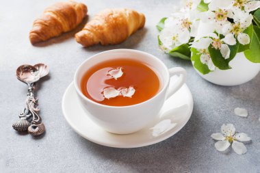 Çay ve kruvasan fincan, gri beton arka plan üzerinde Elma dalı çiçeklenme. Konsept sabah Kahvaltısı.