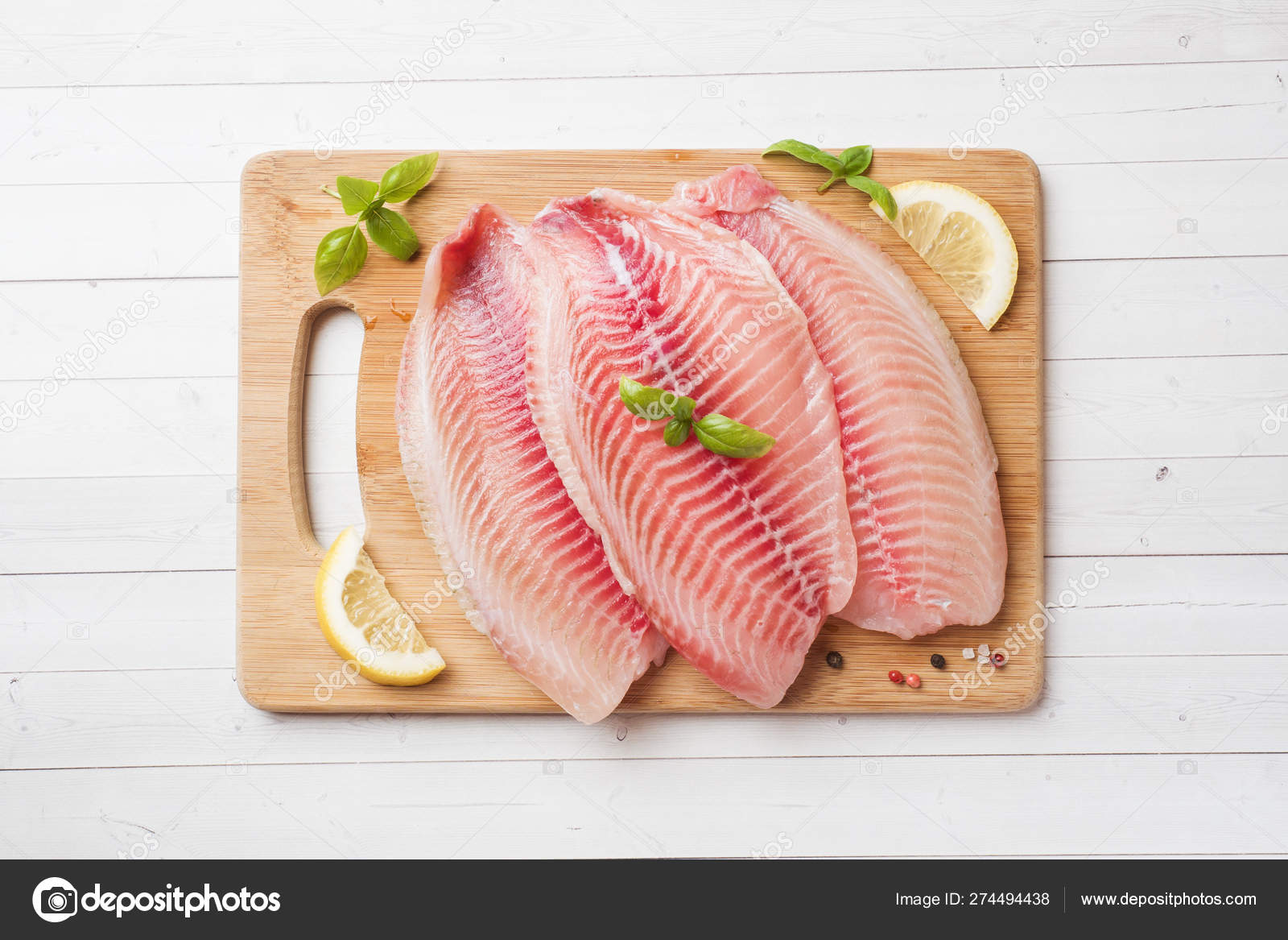 Raw fish fillet of tilapia on a cutting Board with lemon and spices. White  table with copy space. Stock Photo by ©elenglush 274494438