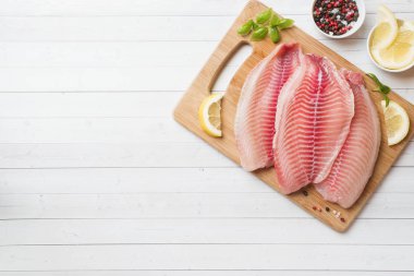 Limon ve baharatlarla bir kesme tahtasında tilapia çiğ balık fileto. Kopya alanı olan beyaz tablo.