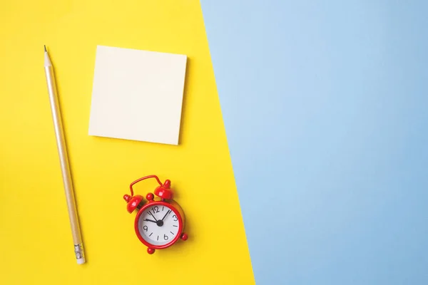 Papelaria de etiquetas e um relógio em uma mesa azul amarela com uma cópia do espaço. Conceito educação escolar, escritório e freelancer . — Fotografia de Stock