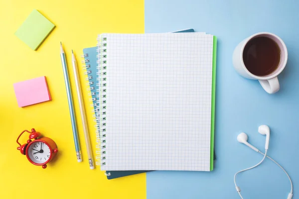 Καθαρίστε το σημειωματάριο και το μολύβι φλιτζάνι καφέ και ένα ρολόι με χώρο αντιγραφής σε κίτρινο μπλε φόντο τραπεζιού για παρουσίαση, συγγραφέα ή σχολική εκπαίδευση, blogger, μυθιστόρημα και τριβή ή έννοια ιστορίας μάρκας. — Φωτογραφία Αρχείου