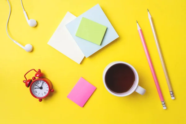 Papelaria de etiquetas diferentes, uma xícara de café e um relógio em uma mesa amarela com uma cópia do espaço. Conceito educação escolar, escritório e freelancer . — Fotografia de Stock