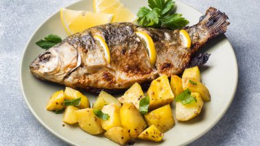 Fırında Balık sazan limon yeşillik ve patates bir plaka üzerinde.