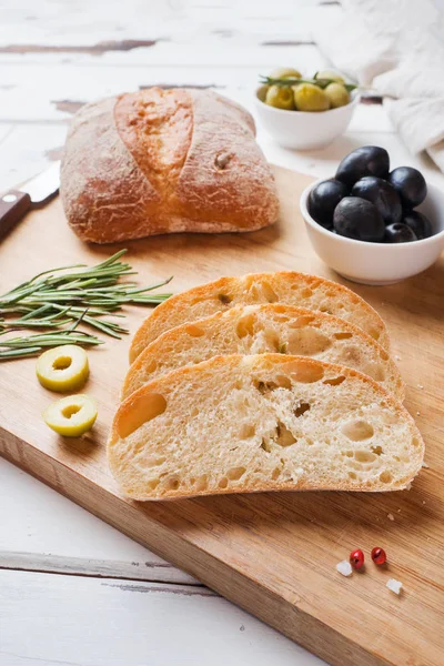 Italienisches Ciabatta-Brot mit Oliven und Rosmarin auf einem Holzbrett. — Stockfoto