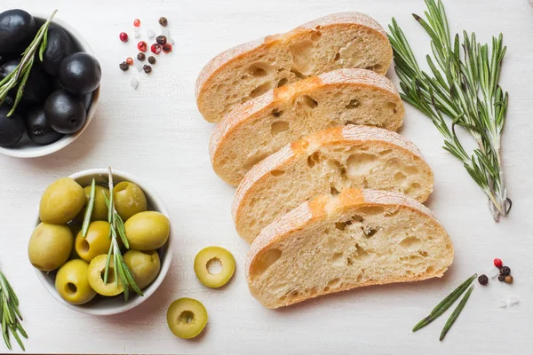 Pão ciabatta italiano com azeitonas e alecrim em uma tábua de corte. fundo de concreto escuro . — Fotografia de Stock