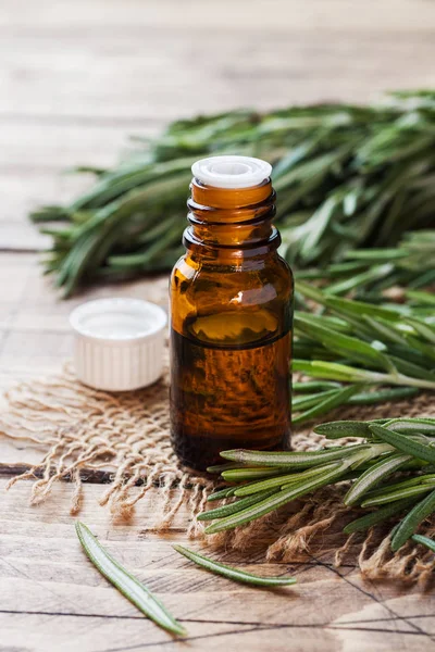Rosemary essential oil in a glass bottle with fresh branch rosemary herb on wooden table for spa,aromatherapy and bodycare.Copy space.