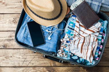 Seyahat hazırlıkları konseptiyle bavul, giysi ve aksesuarları eski ahşap masa. Üstten Görünüm kopya alanı