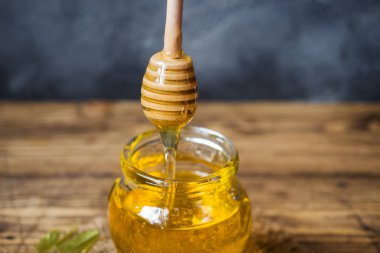 Ihlamur çiçeklerinden bir kavanoz sıvı bal ve koyu renkli bir arka plan üzerinde bal olan bir çubuk. Kopyalama alanı