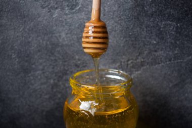 Ihlamur çiçeklerinden bir kavanoz sıvı bal ve koyu bir arka plan üzerinde bal ile bir sopa.