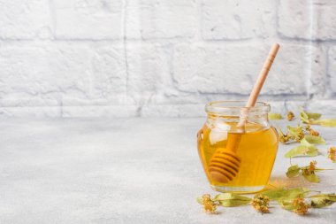 Ihlamur çiçek ve gri beton arka plan üzerinde bir sopa sıvı bal kavanoz. Kopyalama alanı.