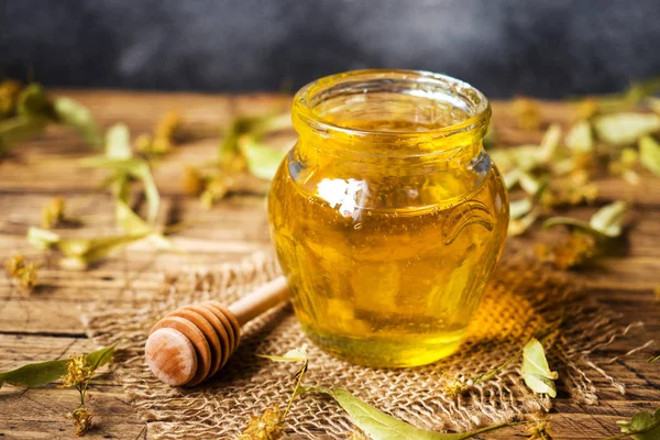 A jar of liquid honey from Linden flowers and a stick with honey on a dark background. — Stock Photo, Image