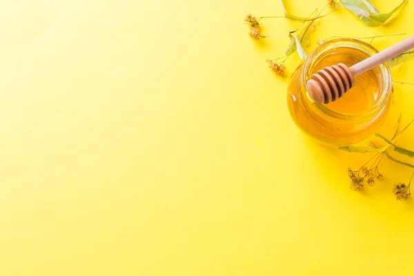 Un barattolo di miele liquido da fiori di tiglio e un bastone con miele su sfondo giallo. Copia spazio — Foto Stock