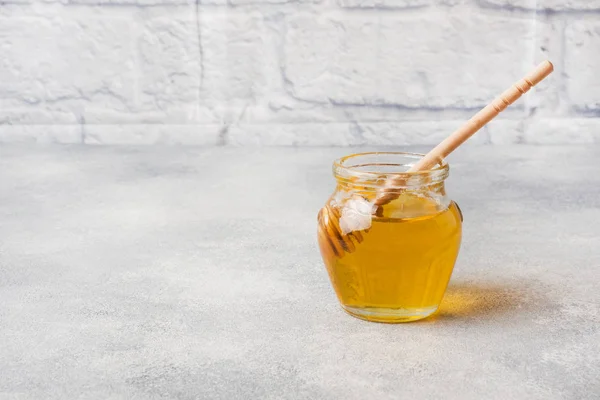 Vaso di miele liquido e bastone su fondo grigio cemento. Copia spazio . — Foto Stock