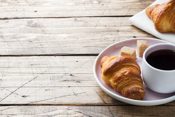 Desayuno cruasanes en un plato y una taza de café, fondo de madera, espacio para copiar . — Foto de Stock