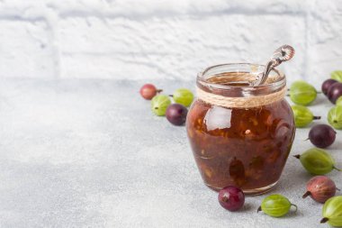 Gri bir arka plan üzerinde taze bektaşi üzümü çilek ile bir kavanozda bektaşi üzümü reçeli. Kopyalama alanı.