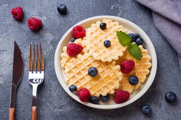 Koyu beton arka plan üzerinde taze ahududu ve yaban mersini ile oluklu waffle çerezleri. Kopyalama alanı.