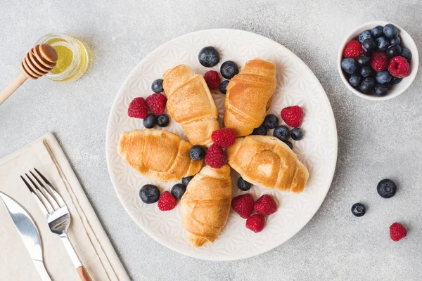 Croissants con frambuesas frescas y arándanos sobre un fondo de hormigón oscuro. Copiar espacio. concepto de desayuno café miel . — Foto de Stock