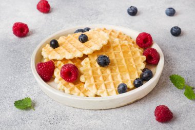 Beton bir arka plan üzerinde taze ahududu ve yaban mersini ile oluklu waffle çerezleri. Kopyalama alanı.