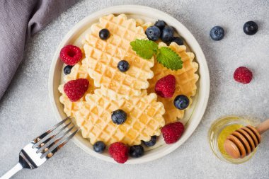 Beton bir arka plan üzerinde taze ahududu ve yaban mersini ile oluklu waffle çerezleri. Kopyalama alanı.