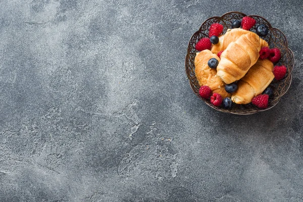 Croissants con frambuesas frescas y arándanos sobre un fondo de hormigón oscuro. Copiar espacio. concepto de desayuno café miel . — Foto de Stock