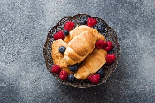 Croissants con frambuesas frescas y arándanos sobre un fondo de hormigón oscuro. Copiar espacio. concepto de desayuno café miel . — Foto de Stock