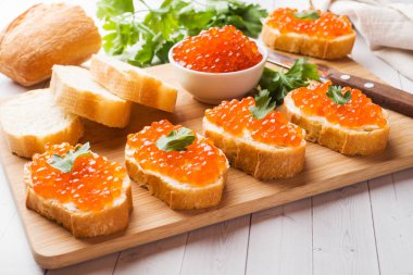 Bir ahşap tahta üzerinde kırmızı somon havyar ile sandviçler. Beyaz masa üstü.