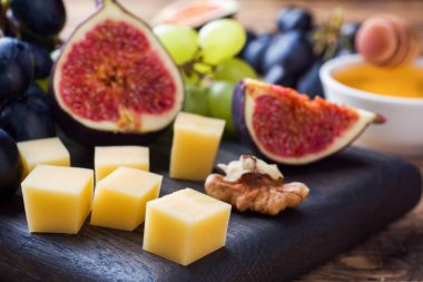 Peynir küpleri, taze meyve inciri üzümleri ahşap kesim tahtasında bal cevizi. Seçici odaklanma. Kapat..