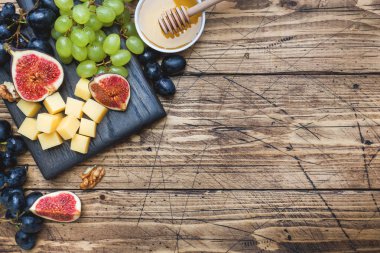 Peynir küpleri, taze meyve inciri üzümleri ahşap kesim tahtasında bal cevizi. Boşluğu kopyala.