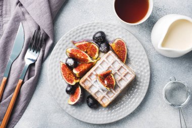 Geleneksel Belçika waffleları, pudra şekerli üzüm ve incir. Ev yapımı sıcak bir kahvaltı. Gri beton arka plan. Boşluğu kopyala.