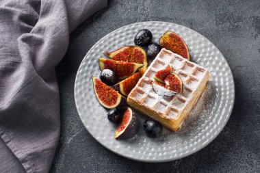 Geleneksel Belçika waffleları, pudra şekerli üzüm ve incir. Ev yapımı sıcak bir kahvaltı. Gri beton arka plan. Boşluğu kopyala.