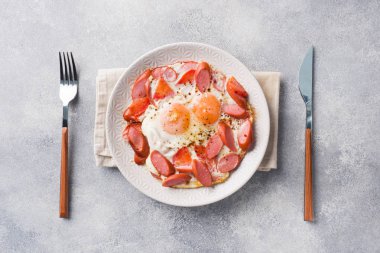 Kızarmış yumurta sosis ve domates masada bir tabakta. Zengin ev yapımı kahvaltı. Gri beton arka plan. Kopyalama alanı.