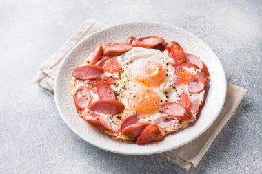 Kızarmış yumurta sosis ve domates masada bir tabakta. Zengin ev yapımı kahvaltı. Gri beton arka plan. Kopyalama alanı.