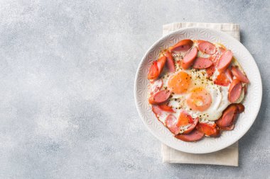 Kızarmış yumurta sosis ve domates masada bir tabakta. Zengin ev yapımı kahvaltı. Gri beton arka plan. Kopyalama alanı.